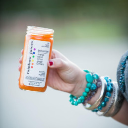 A hand with numerous bracelets around their wrist holds out a Bohemian juice from Rainbow Juices