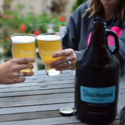 Two people bringing their Beachwood Brewing glasses together in a cheers