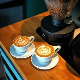 Two foamed coffee drinks on a wooden counter
