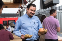 A smiling man holds up a plate of fries in one hand and a fried chicken sandwich in the other.